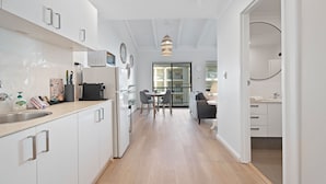 A modern kitchen with white cabinets, a dining area with a table and chairs, and a view to a balcony.