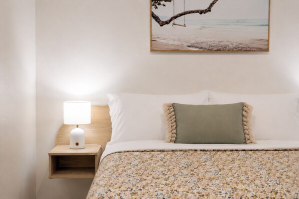 A neatly made bed with a floral-patterned bedspread, a green pillow, and a white pillow. A wooden nightstand with a white lamp is to the left. - Scarborough Beach Escape NEW (Scarborough)