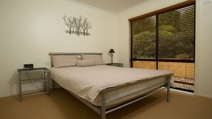 Quarto com estrutura de cama de metal, mesa de cabeceira com abajur, régua de tomadas e uma obra de arte na parede.