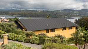 Um edifício amarelo com telhado inclinado, rodeado por vegetação exuberante e vista para um lago.