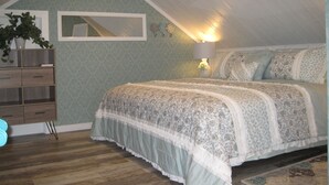A bedroom with a sloped ceiling, a bed with patterned bedding, a bedside lamp, a dresser, and a potted plant. - Private Spacious Unit. King bed/2 twin xl beds (Citrus Heights)