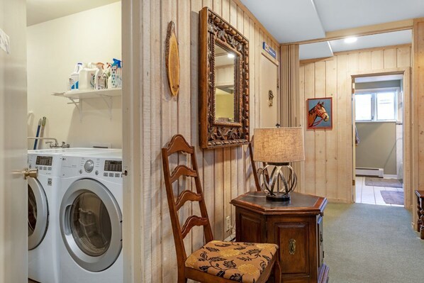 A laundry area with a washing machine, a wooden chair, a mirror, and a lamp.