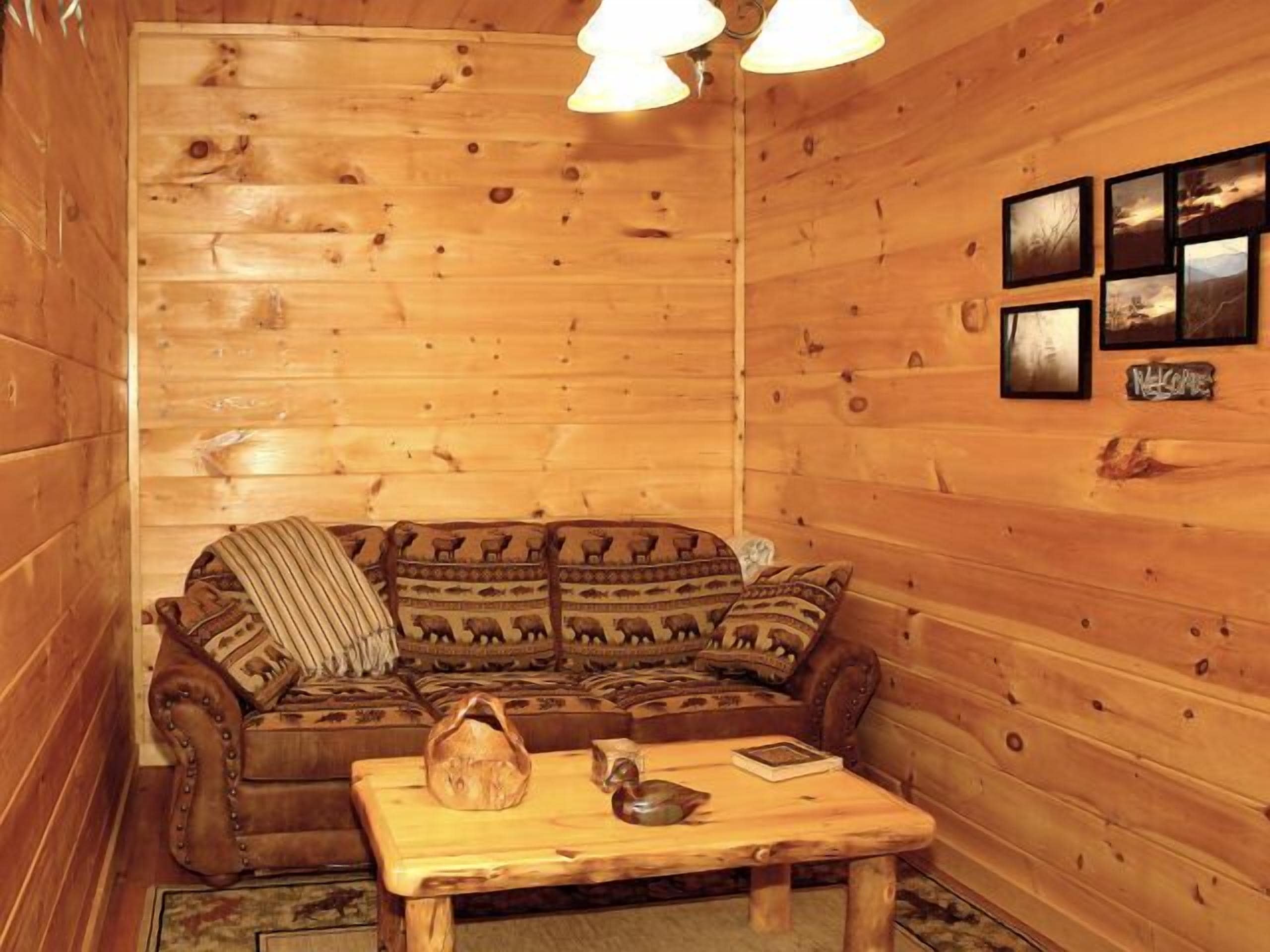 A cozy cabin interior with a wooden sofa, a small table, and framed pictures on the wall.