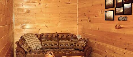 A cozy cabin interior with a wooden sofa, a small table, and framed pictures on the wall.