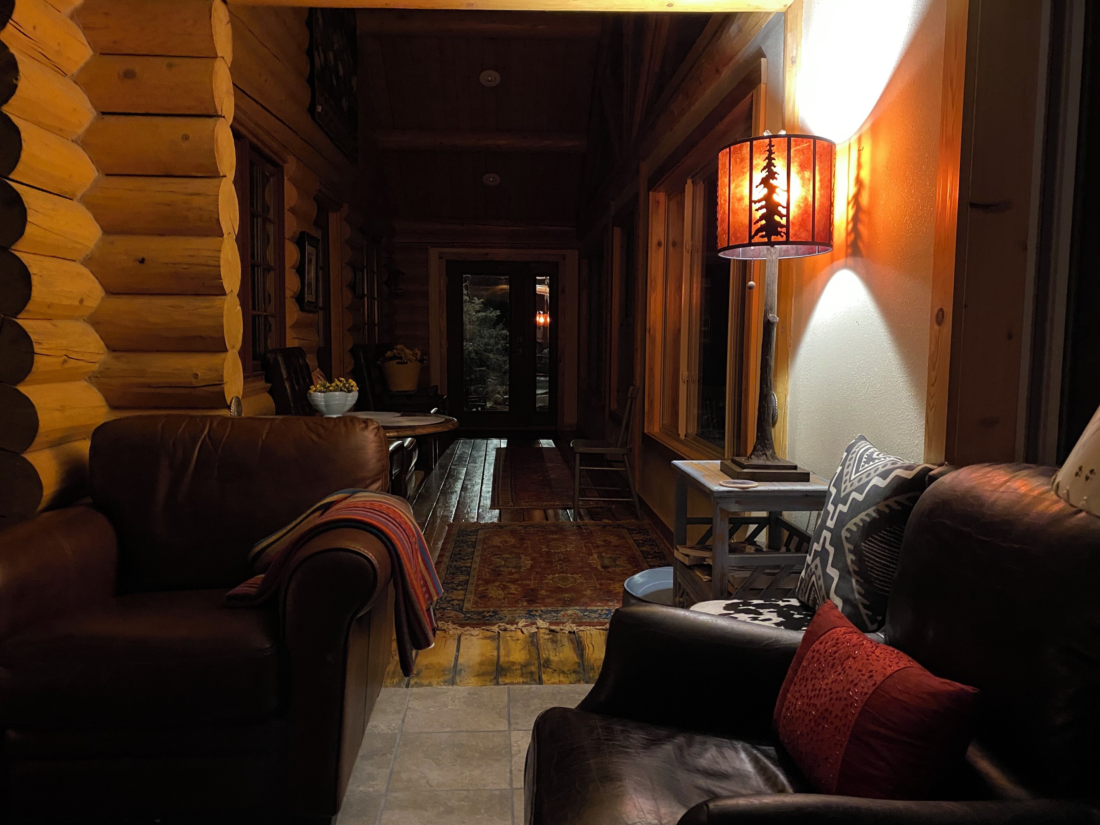 L’intérieur d’un chalet confortable, avec des murs en rondins de bois, un canapé en cuir, une table à manger en bois et une lampe décorée d’un motif d’arbre.