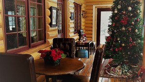 Interior de una cabaña de troncos con comedor, pisos de madera y un árbol de Navidad decorado.