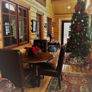 Interno di una baita in legno con zona pranzo, pavimento in legno e albero di Natale decorato.