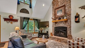 Un salon chaleureux avec une cheminée en pierre, un canapé en cuir, des fauteuils à motifs et un téléviseur à écran plat.