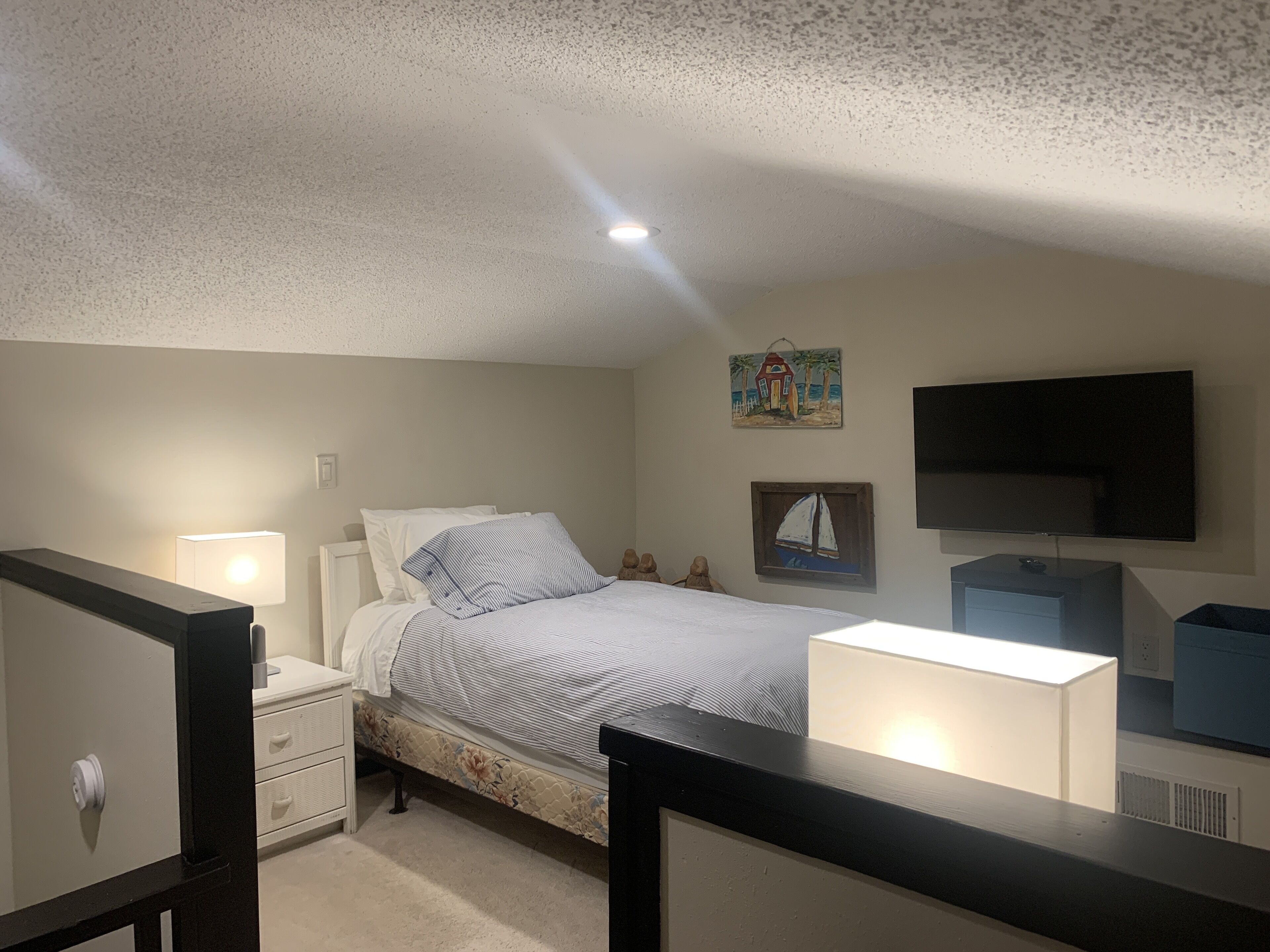 A bedroom with a bed, nightstand, dresser, and a TV mounted on the wall.