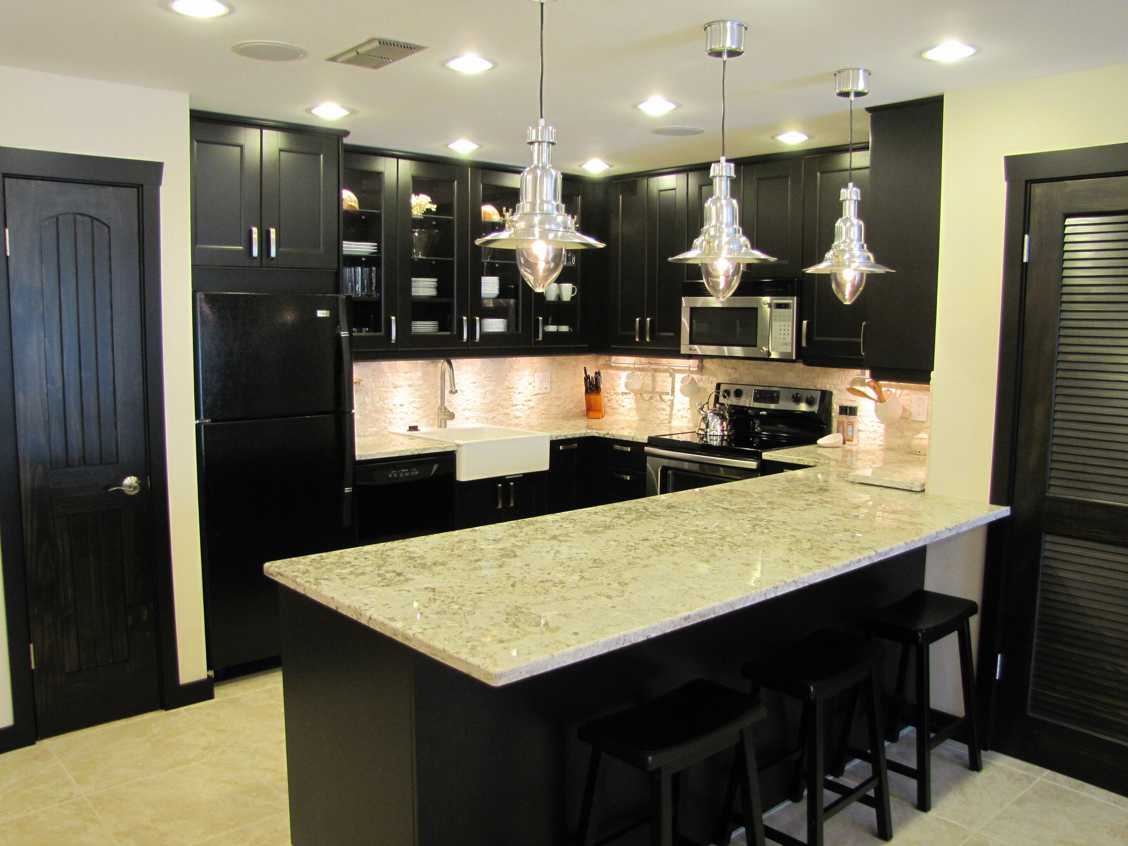 A modern kitchen with dark cabinetry, a large island with bar stools, stainless steel appliances, and pendant lighting.