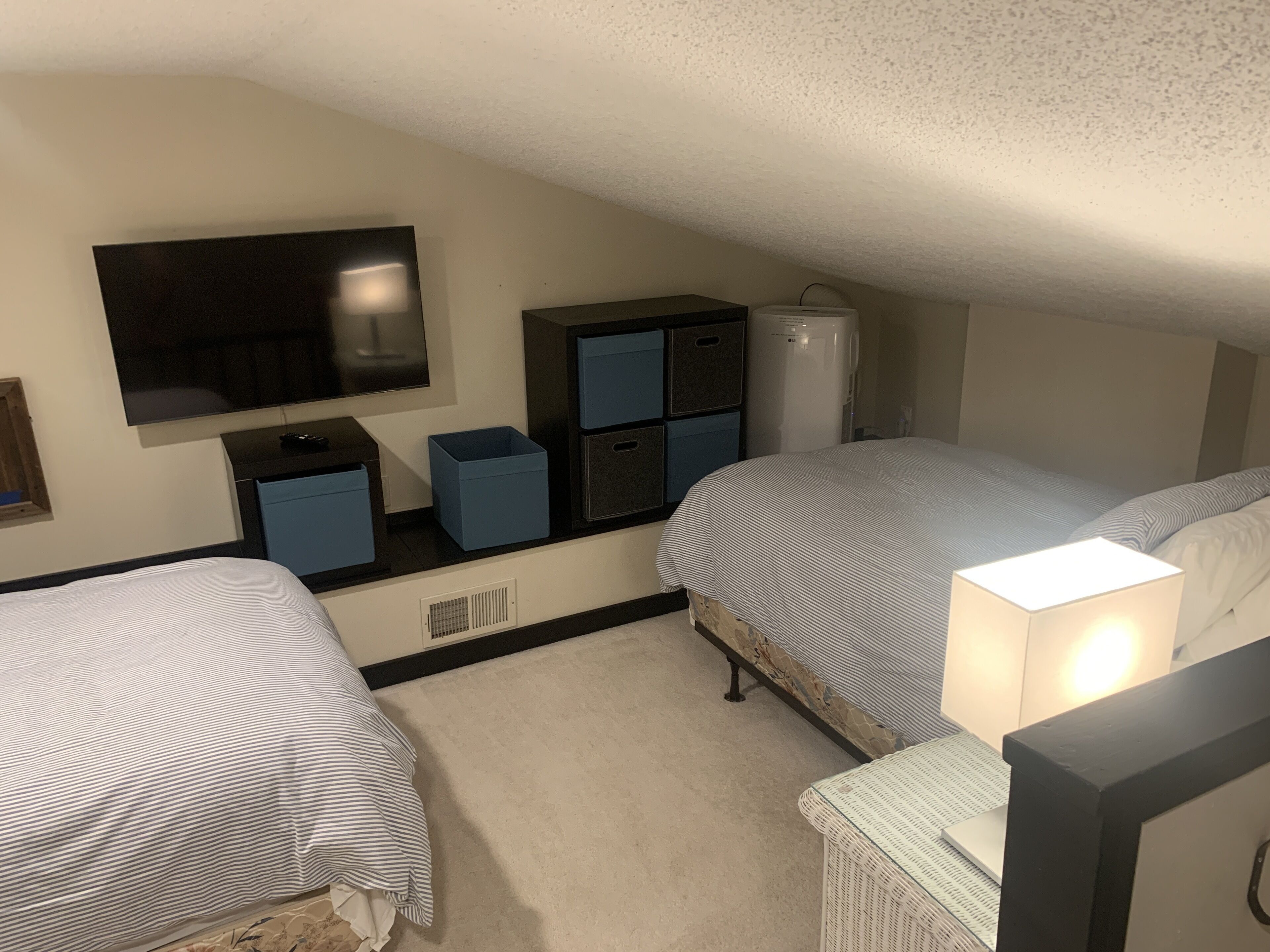 A bedroom with two beds, a TV, storage units, and a radiator.