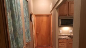 A narrow hallway with wooden flooring, a wooden door at the end, and a kitchen area with wooden cabinets and a microwave. - BEAUTIFUL SPACIOUS APARTMENT- 1 Bedroom with Living Room & Kitchen. Sleeps 4. (Monument)