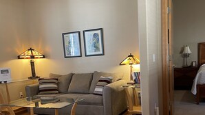 A living room with a sofa, two lamps, a glass coffee table, and wooden flooring. - BEAUTIFUL SPACIOUS APARTMENT- 1 Bedroom with Living Room & Kitchen. Sleeps 4. (Monument)