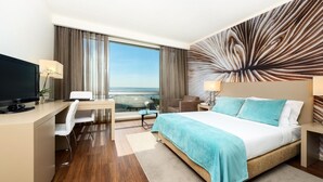 Habitación de hotel moderna con una cama grande, un escritorio con computadora, una silla y vista al mar a través de amplios ventanales.