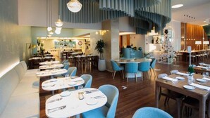 Un interior de restaurante moderno con mesas redondas, sillas azules y lámparas colgantes.