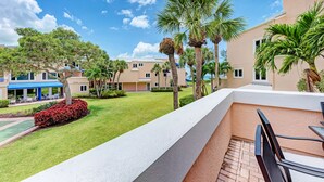 A balcony with a view of a well-maintained lawn, palm trees, and a building with a blue awning. - Unit #207 Sand Cay Beach Resort Pool View (Longboat Key)