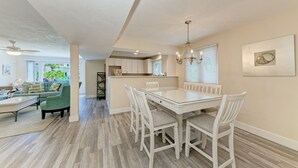 A spacious living area with a glass-top dining table, white chairs, and a green sofa.