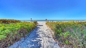 A sandy path leading to beach chairs and a trash bin, surrounded by green vegetation. - Unit #207 Sand Cay Beach Resort Pool View (Longboat Key)