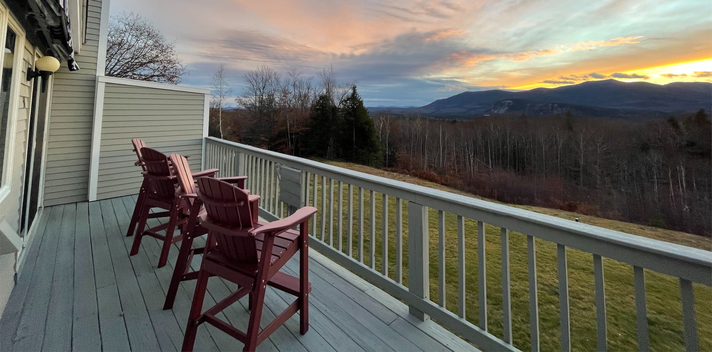 A wooden deck with Adirondack chairs overlooking a mountainous landscape.