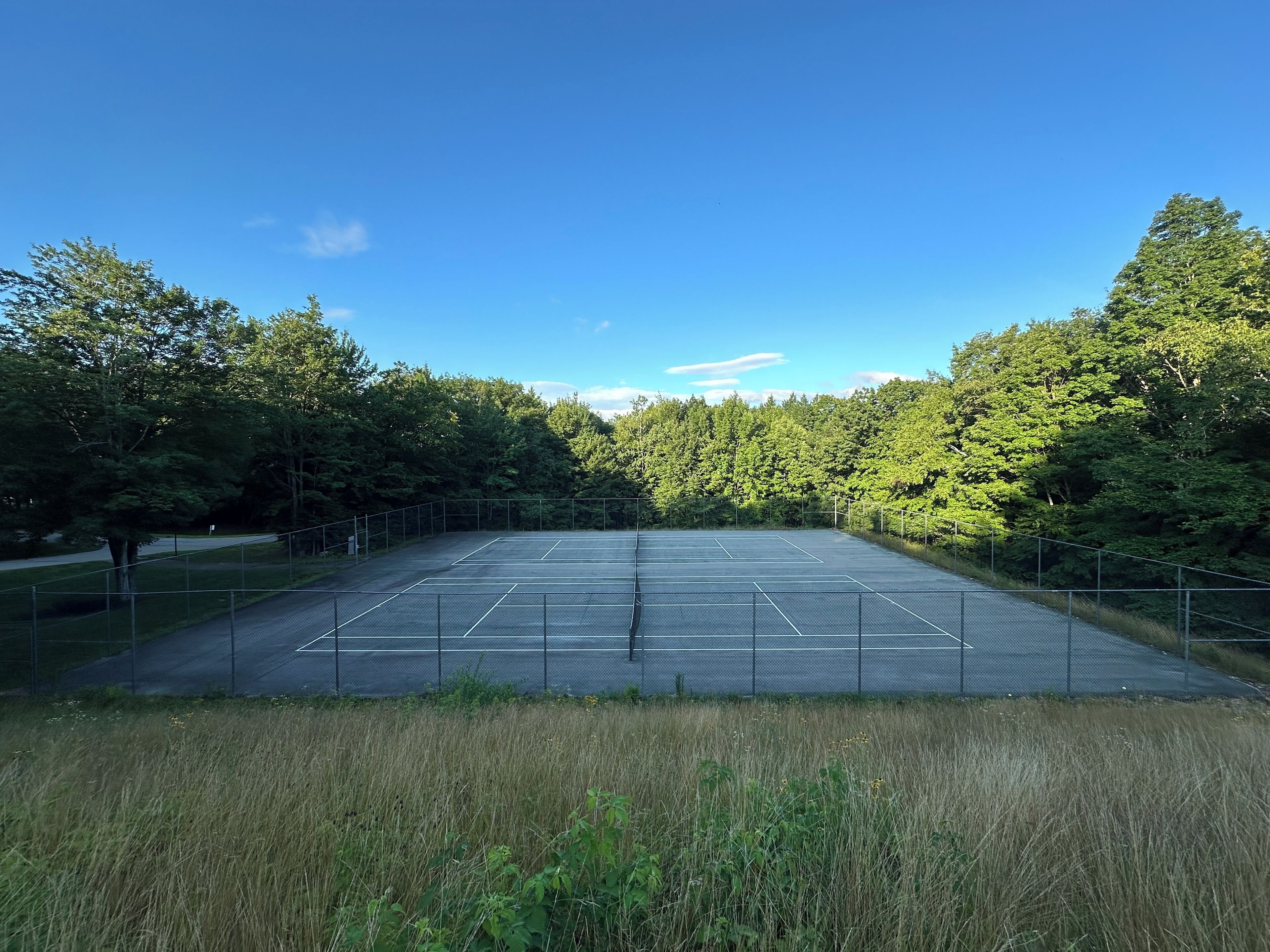 An outdoor tennis court surrounded by trees.
