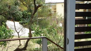 A wooden deck with a round table and a chair, surrounded by a metal fence and trees. - Central location - walking distance to beaches, shops and hotel. (Point Lookout)