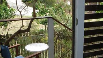 A wooden deck with a round table and a chair, surrounded by a metal fence and trees.