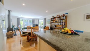 Uma cozinha moderna com bancada de granito, cadeiras de madeira, uma mesa de jantar e uma estante repleta de livros.