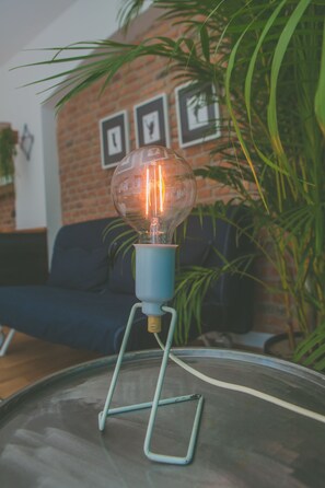 A clear glass bulb lamp on a metal stand in a room with a brick wall and framed pictures. - Projekt Piekary (Poznan)