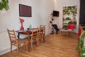 A dining area with a wooden table and chairs, a red lamp, and a bookshelf with plants. - Projekt Piekary (Poznan)