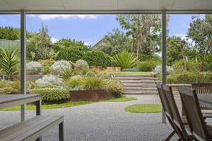 A covered outdoor area with a gravel path, wooden benches, and a variety of plants and trees.