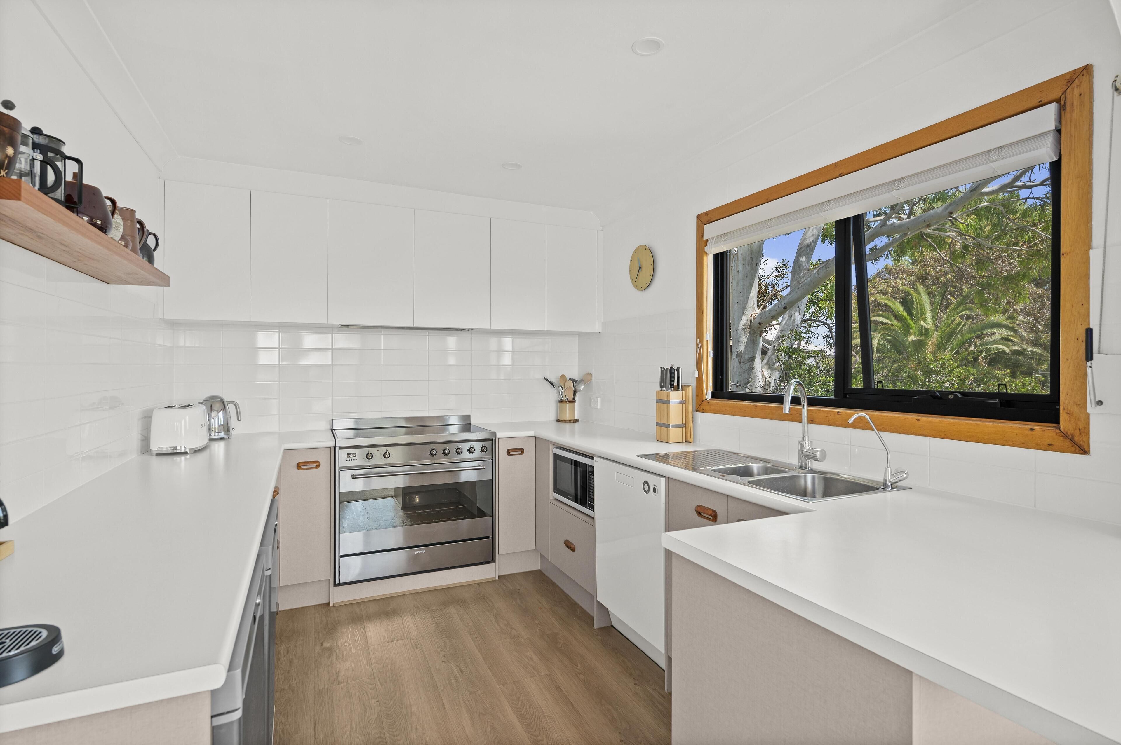 A modern kitchen with white cabinetry, stainless steel appliances, and a window with a view of greenery.