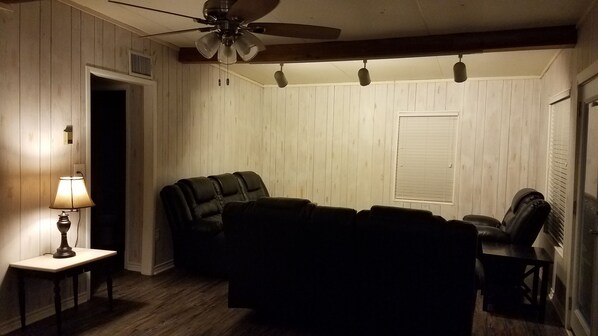 A living room with a ceiling fan, a sofa, a table with a lamp, and a window with blinds.