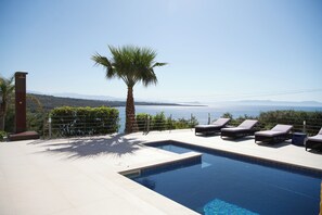A swimming pool with lounge chairs and a palm tree, overlooking a body of water and distant mountains. - Yellow Dream Villas - Sunset villa (Chorafakia, Chania Crete)