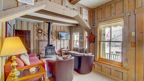 A cozy room with a fireplace, wooden walls, a sofa, and a large window. - Park City Base - Walking Distance from Downtown + Comfortable, Cozy & Pet Friendly Home! (Park City)