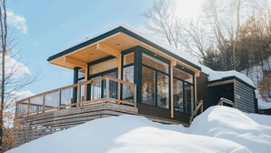 Een moderne chalet met grote ramen, een houten terras en een besneeerd landschap.