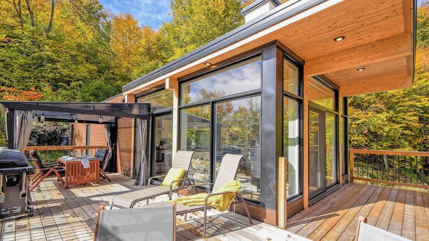 Een modern terras buiten met zitplaatsen, een barbecue en grote ramen.