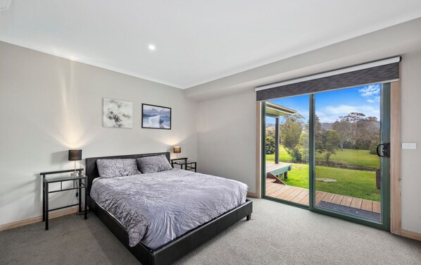 A bedroom with a bed, bedside tables, and a view of a garden through a sliding glass door. - Silkwood on the Goulburn  (Eildon)