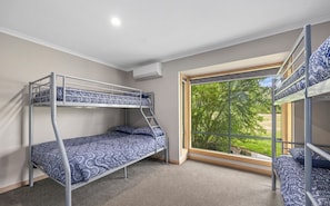 Habitación con literas, ropa de cama estampada, ventana con vistas a la vegetación y aire acondicionado.