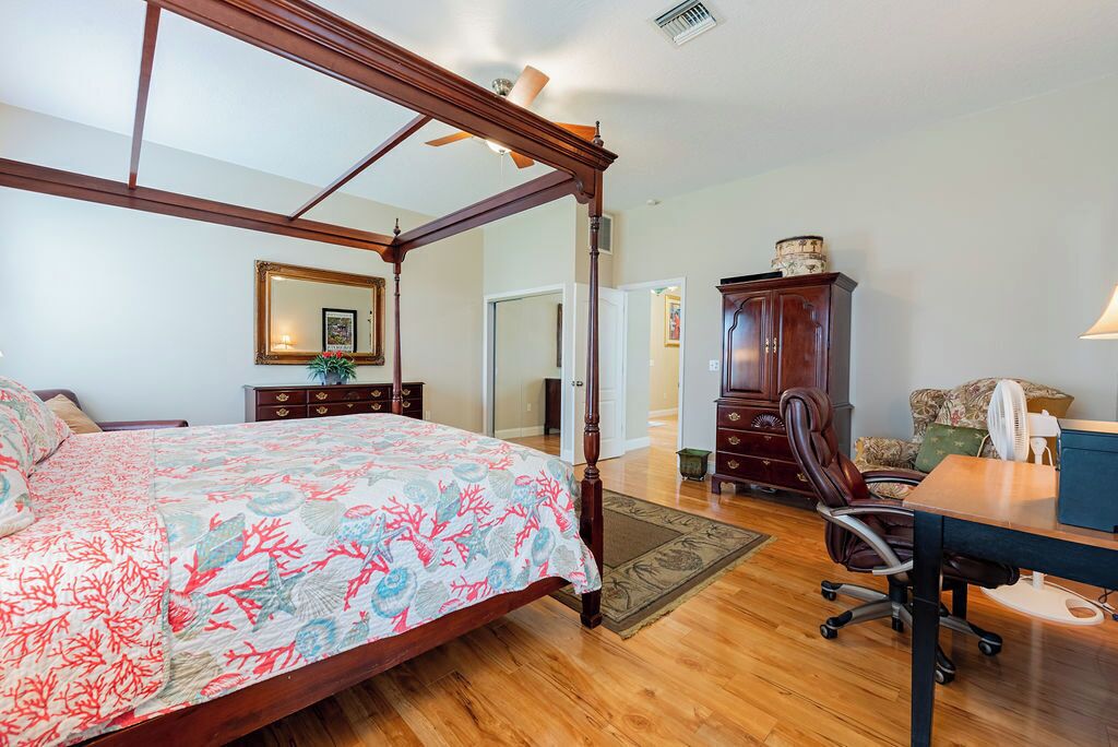 A bedroom with a four-poster bed, a wooden desk, a chair, a cabinet, and a mirror.