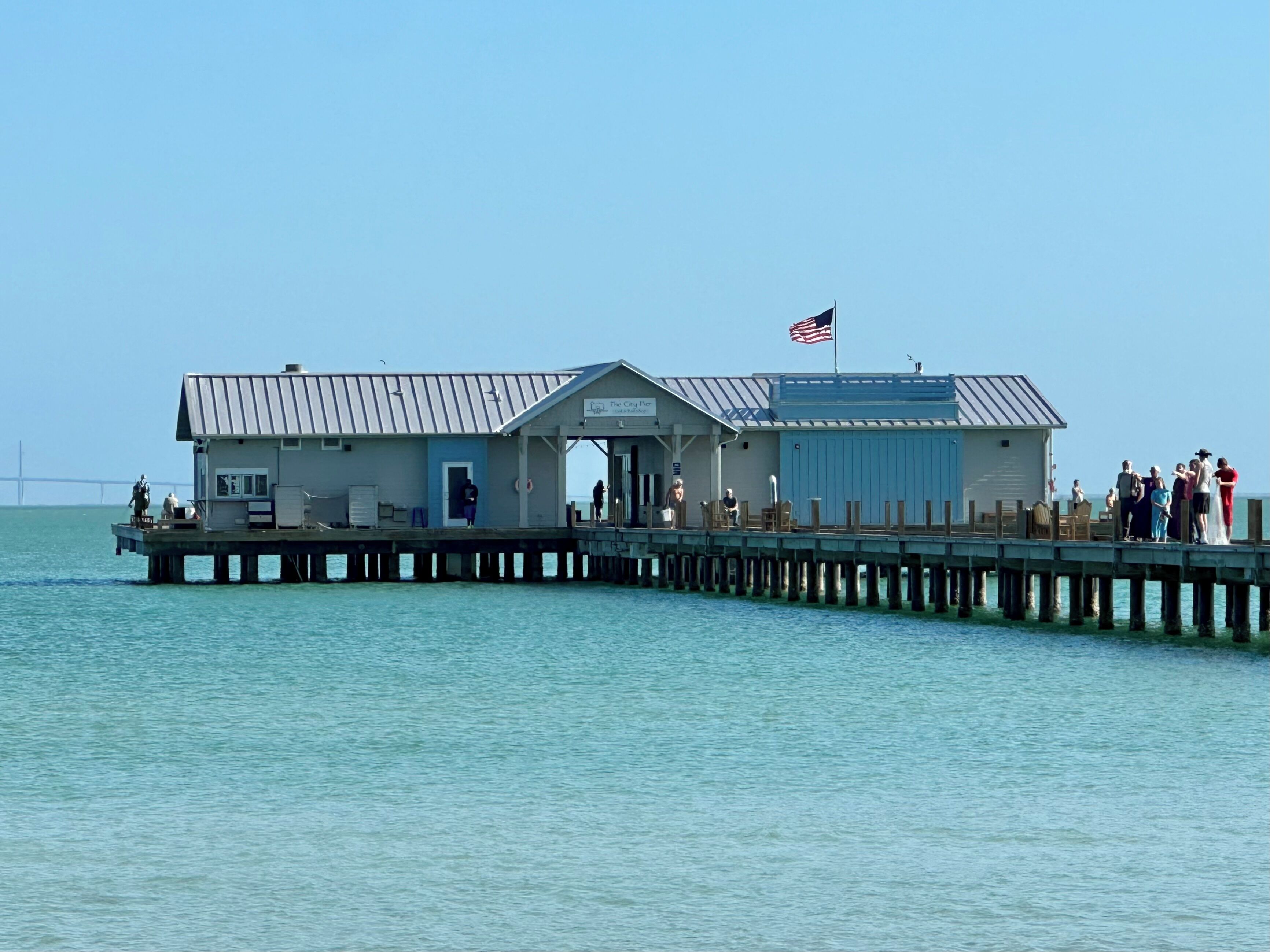 A pier with a small building, a flag, and people.