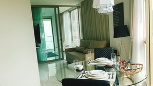 Un espace repas moderne avec une table en verre pour deux personnes, un canapé et une vue sur le balcon extérieur.