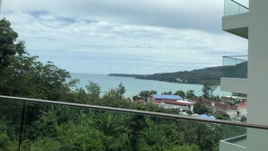 Un balcon offrant une vue sur un paysage côtier, comprenant une étendue d’eau et des collines lointaines.