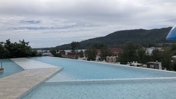 Une piscine dotée d’une terrasse carrelée, entourée de bâtiments et bordée d’un paysage vallonné.