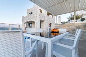 A stone building with arched windows, a table with chairs, and a view of the sea. - Villa Ovgoro – Luxury 3-Level Villa with Heated Pool, Jacuzzi & Panoramic Views (Kamilari)