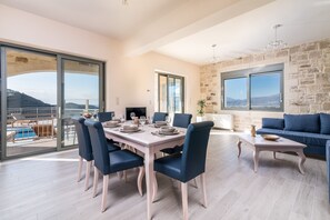 A dining area with a table set for six, a blue sofa, and a stone wall. - Villa Ovgoro – Luxury 3-Level Villa with Heated Pool, Jacuzzi & Panoramic Views (Kamilari)