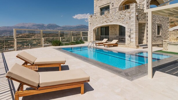 Une villa en pierre dotée d’une piscine, de chaises longues et offrant une vue sur les montagnes.