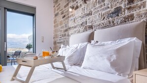 Une chambre avec un mur en pierre, un lit recouvert de draps blancs, une table de chevet et une fenêtre donnant sur un beau paysage.