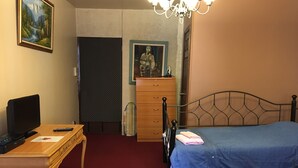 Une chambre à coucher avec un lit, un bureau avec un ordinateur et une télévision, une commode et un tableau accroché au mur.