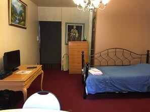 Ein Schlafzimmer mit einem Bett, einem Schreibtisch mit Computer und Fernseher, einer Kommode und einem Bild an der Wand.