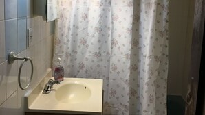 Une salle de bain équipée d’un lavabo, d’un miroir, d’un porte-serviettes, d’un rideau de douche et d’un luminaire fixé au mur.